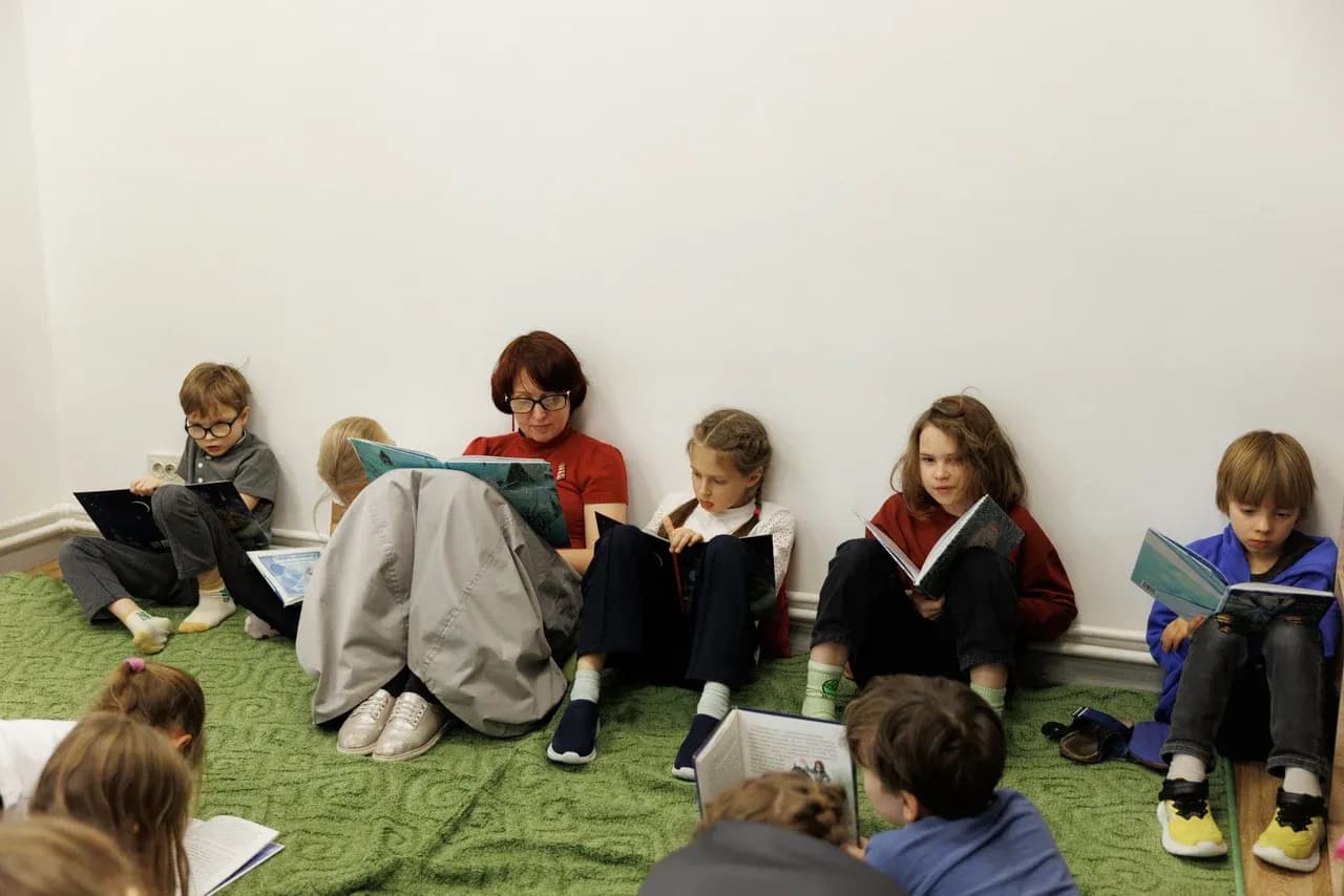 Дети и педагог читают книги, сидя на ковре